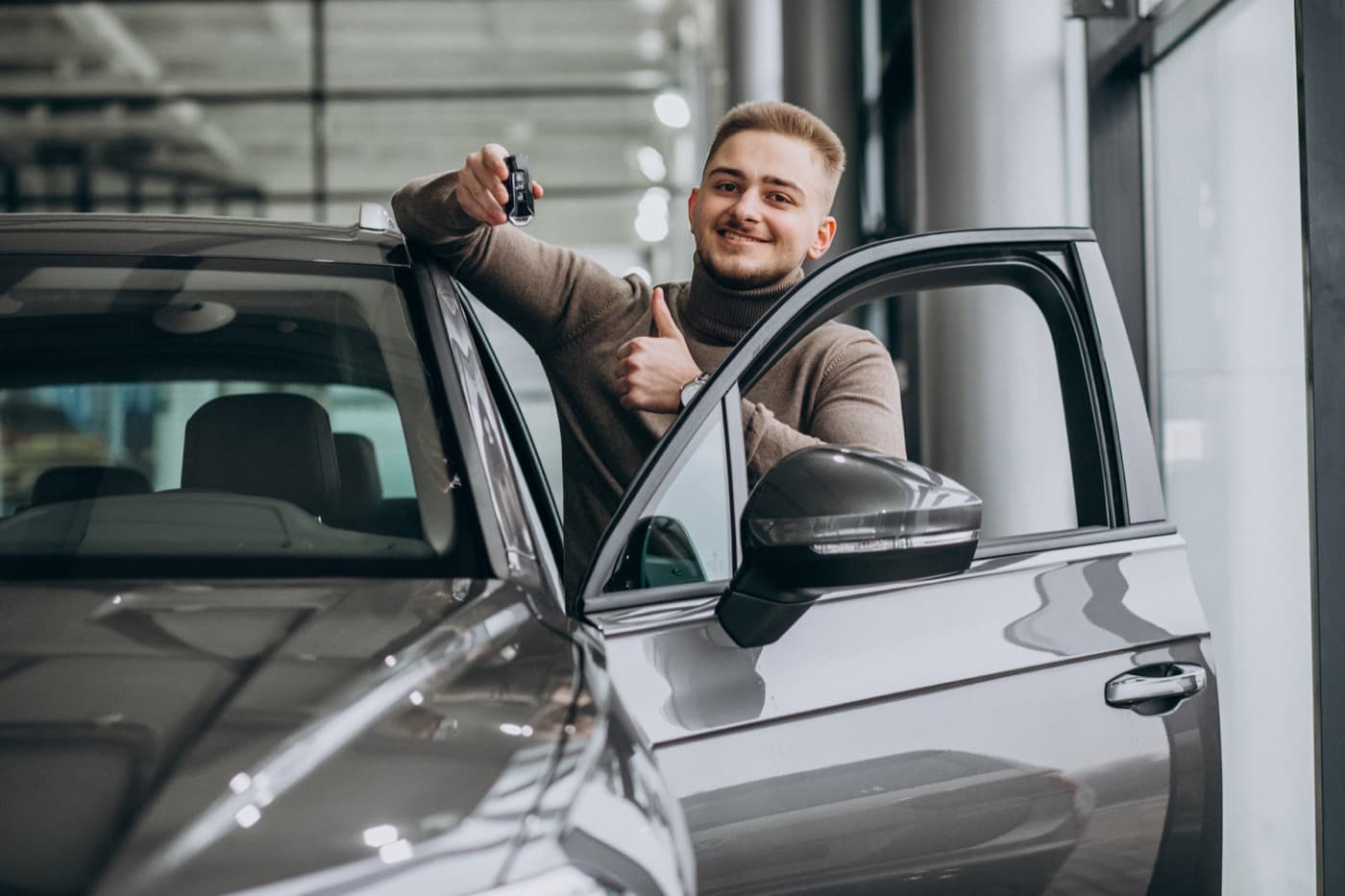 Happy man holding car keys at dealership